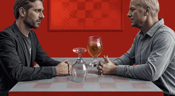 Dwóch mężczyzn siedzi przy stole. Jeden pije piwo, drugi ma pusty kieliszek. Trudne rozmowy o życiu z alkoholikiem niepijącym.