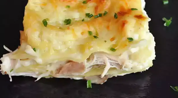 Une part de lasagnes poulet champignons, gratinée et garnie de persil frais, sur une assiette noire.