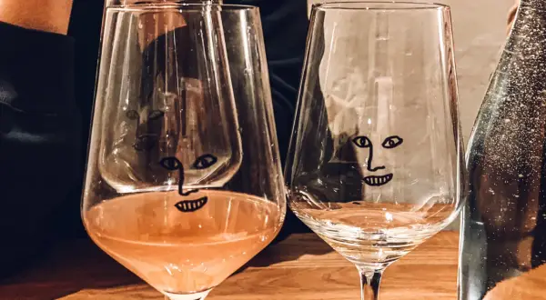 Dwa kieliszki z zabawnymi buźkami na drewnianym stole w wine barze w Gdańsku. Jeden z nich zawiera różowe wino.