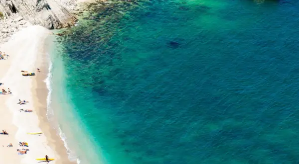 Spiaggia dorata e mare cristallino, con kayak gialli e persone che si godono il sole. Un angolo di paradiso che ricorda il **gradara mare**.