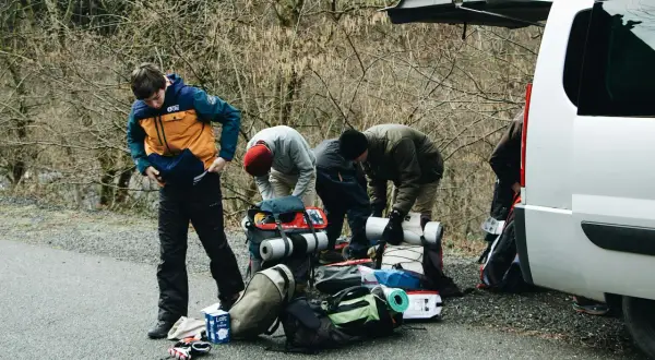 Przygotowania do wyprawy w Tatry w listopadzie. Grupa ludzi pakuje sprzęt turystyczny przy otwartym bagażniku białego vana.