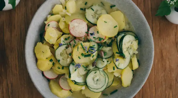 Ein Teller mit traditionellem bayrischem Kartoffelsalat, garniert mit Radieschen, Gurken und Schnittlauch.