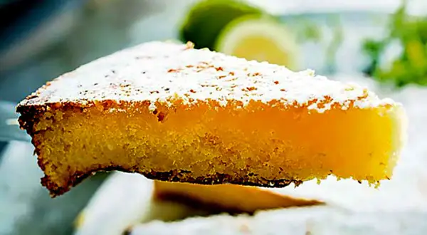 Una fetta di torta caprese al limone, spolverata di zucchero a velo, con fette di limone sullo sfondo.
