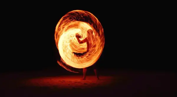 A performer creates a fiery vortex with a poi in this stunning fire photography. The flames swirl around them, illuminating the dark night.