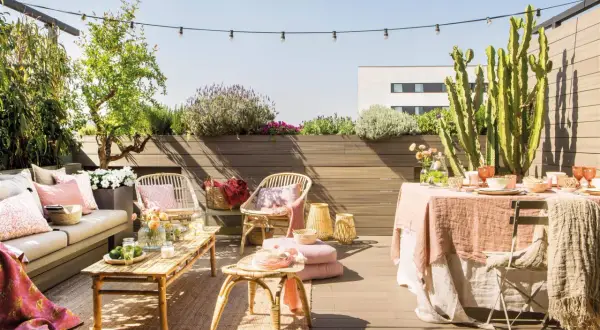 Terraza de ático lista para disfrutar. Una reforma que invita a la relajación con mobiliario de ratán, textiles suaves y plantas exuberantes.