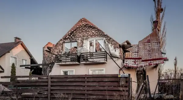 Zniszczony dom po ostrzale. Rozbiórka dachu i ścian, wybite okna, zniszczony płot.