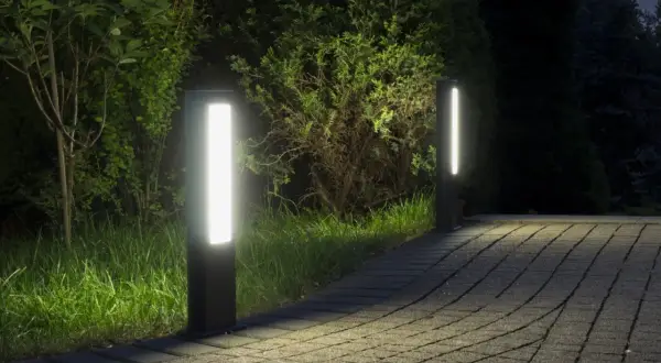 Dwa nowoczesne słupki LED oświetlają ścieżkę z kostki brukowej w ogrodzie.