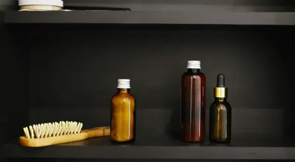 Holzhaarbürste und braune Fläschchen auf dunkler Ablage. Mögliche Pirocton-Olamine-Nebenwirkungen bei der Anwendung von Kosmetika.
