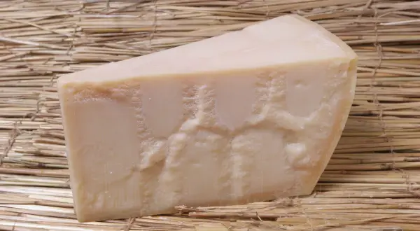 En bit Grana Padano parmesanost ligger på en bädd av halm.