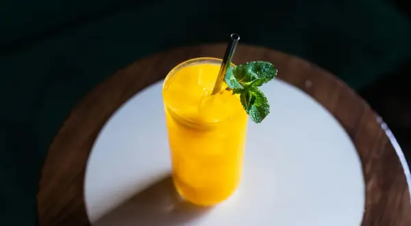 Orzeźwiający drink z mango, z kostkami lodu i listkiem mięty, podany w szklance ze słomką.