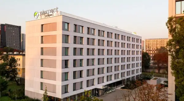 Nowoczesny hotel Element by Westin z zielonym logo na dachu, otoczony drzewami i innymi budynkami.