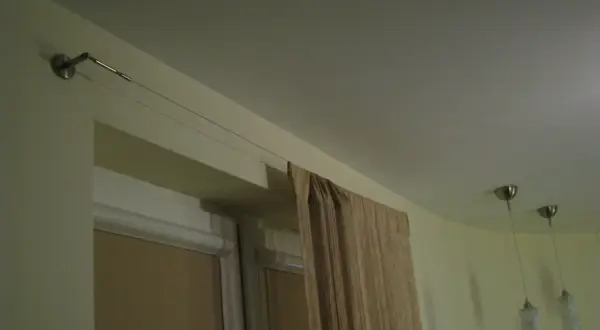 Elegancka zasłona w beżowym kolorze wisi na cienkiej lince zamiast karnisza, tworząc minimalistyczny wygląd.