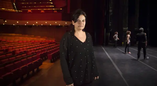 Emma Dante in un teatro, con le poltrone rosse vuote e il palco illuminato.
