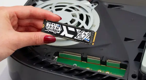 Dłoń z czerwonym lakierem trzyma dysk SSD M.2 PCIe 4.0 NVMe, gotowy do montażu w konsoli.