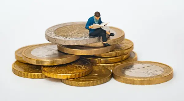 Figurka siedzi na stosie monet, czytając. Jak sprawdzić ile ktoś ma długu? Może warto zacząć od analizy finansów, jak ta figurka analizuje swoje monety.