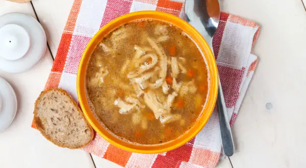 Aromaticzne flaki po zamojsku w pomarańczowej misce, obok kromka chleba i łyżka.