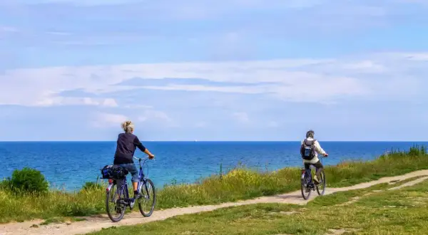 Dwie osoby na rowerach przemierzają malowniczy szlak nadmorski. Błękitne niebo i morze tworzą tło dla tej spokojnej podróży.