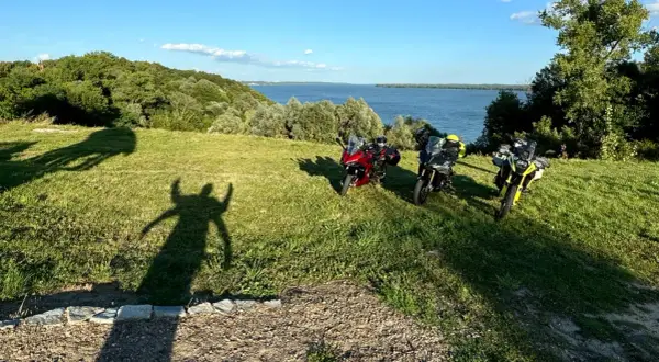 Trzy motocykle na trawiastym wzgórzu z widokiem na jezioro i las.