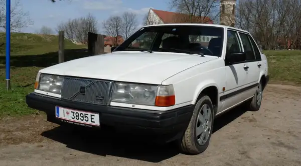 Białe Volvo 840 z przodu, na tle drzew i kościoła.