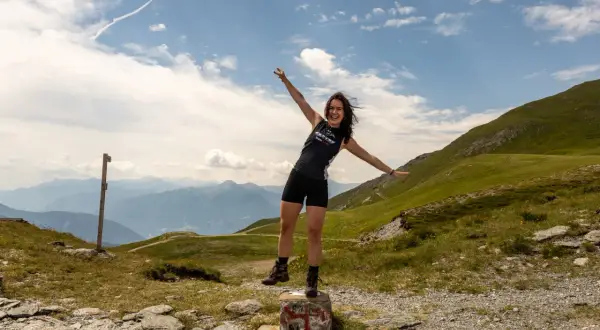 Glückliche Frau mit ausgestreckten Armen auf einem Berg in den Alpen, ein Zeichen für ihr Backpacking Europa Abenteuer.