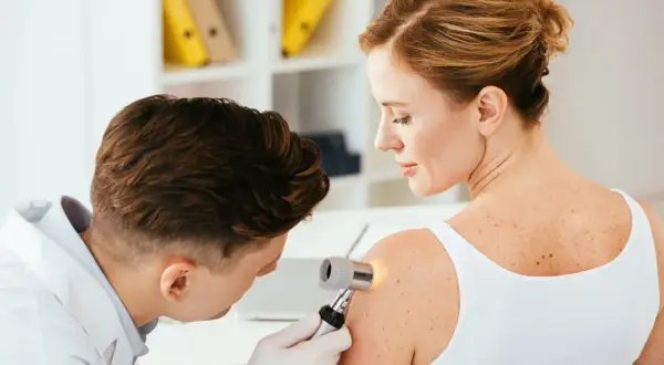 Dermatolog bada pieprzyk na ramieniu pacjentki. Warto pamiętać o samobadaniu skóry, by wcześnie wykryć czerniak na dziąśle lub innym miejscu.