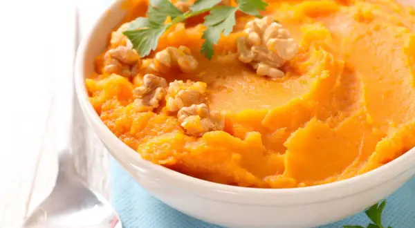 Un bol de purée de patate douce onctueuse, garni de noix croquantes et de persil frais. Un délice réconfortant.