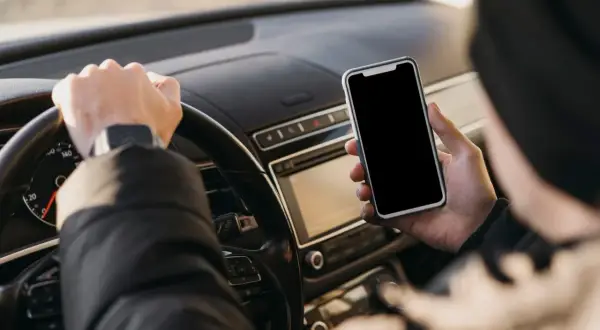 Kierowca trzyma telefon podczas jazdy, ryzykując mandat za korzystanie z telefonu.