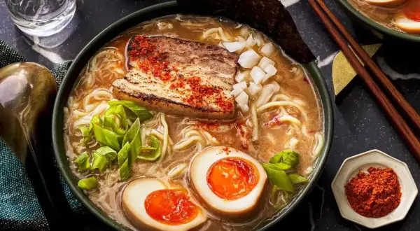 A miska pełna aromatycznego ramen co to jest? Makaron, jajko na pół, kawałek mięsa i szczypiorek w bulionie.
