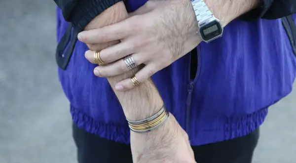 Combinaciones de pulseras y anillos dorados y plateados en brazos y muñecas, con reloj digital.