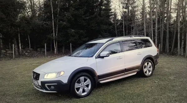 Vit Volvo XC70 parkerad på en gräsmatta med skog i bakgrunden. Kanske ett volvo d4 motor problem gör att den står stilla.