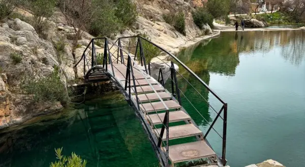 Puente metálico sobre aguas cristalinas, ideal para bolbaite fotos. Rocas y vegetación rodean el estanque.