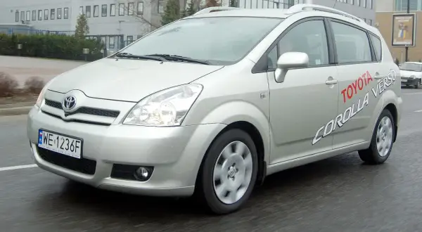 Srebrna Toyota Corolla Verso jedzie po mokrej drodze. Na drzwiach widnieje napis "Toyota Corolla Verso".