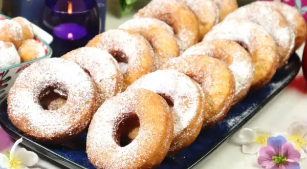 Szybkie oponki w 5 minut, posypane cukrem pudrem, wyglądają apetycznie na niebieskiej tacy. Obok świece i kwiaty.