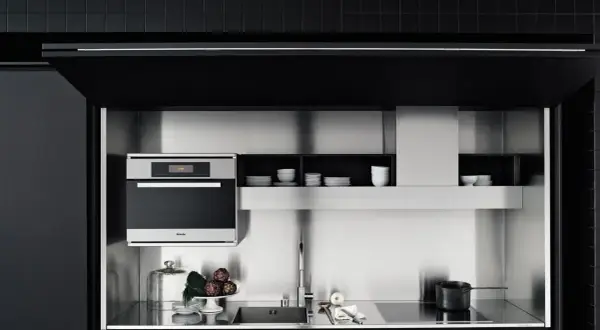 Cocinas invisibles: un horno Miele, fregadero y placa de inducción integrados en un diseño minimalista de acero inoxidable y gabinetes negros.
