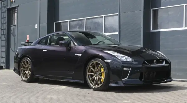 Ciemny Nissan R35 z brązowymi felgami i żółtymi zaciskami hamulcowymi stoi przed szarym budynkiem.