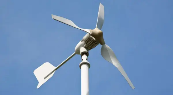 Moja elektrownia wiatrowa, biała turbina z trzema łopatami, obraca się na tle błękitnego nieba, czerpiąc energię z wiatru.