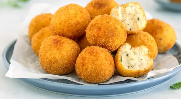 Un piatto di polpette di ricotta dorate e croccanti, alcune intere, altre spezzate per mostrare il ripieno morbido e profumato.