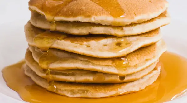 Pila di pancake proteici dorati, inzuppati di sciroppo d'acero che cola.