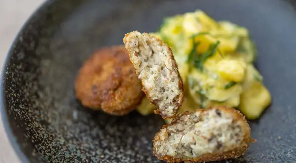 Zwei goldbraune Fischbuletten, eine aufgeschnitten, daneben Kartoffelsalat. Ein leckeres Fischbuletten Rezept.