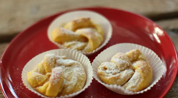 Tre saffransbullar med vit choklad, pudrade med florsocker, ligger på en röd tallrik.
