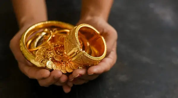 Manos sostienen un tesoro de joyas de oro, pulseras y monedas, un reflejo de las curiosidades del oro y su valor eterno.