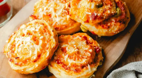 Leckere Pizzaschnecken aus Pizzateig, überbacken mit Käse und Tomaten, liegen auf einem Holzbrett.