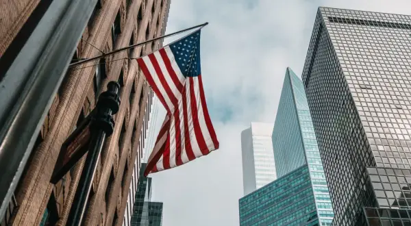 Amerykańska flaga powiewa między drapaczami chmur. Zastanawiasz się, ile kosztuje ubezpieczenie w USA?