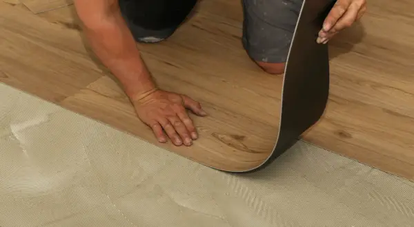 Hand verlegt Laminat auf PVC-Boden. Der Kleber ist auf dem Untergrund aufgetragen, bereit für das neue Bodenmuster.
