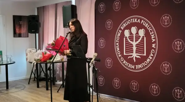Kobieta przemawia na tle baneru z logo biblioteki, podczas wydarzenia w Garwolinie. Wgm rejestracja.