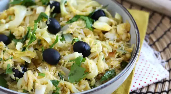 Un plat de bacalhau à bras, mélange savoureux de morue effilochée, d'oignons, d'œufs brouillés et d'olives noires, garni de persil frais.