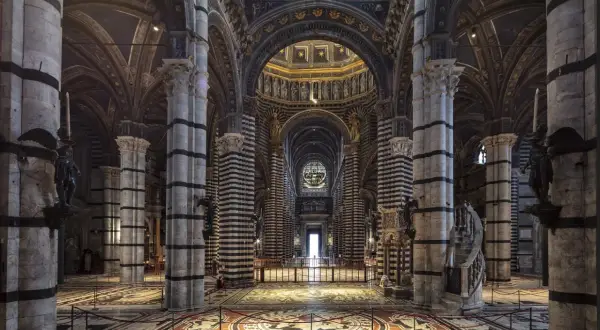 Interno del Duomo di Siena, con il suo magnifico pavimento intarsiato e le colonne a strisce bianche e nere che conducono verso l'altare.