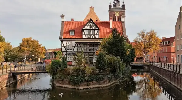 Gdańsk ciekawostki: malowniczy dom z muru pruskiego nad kanałem, w tle wieża kościelna i jesienne drzewa.