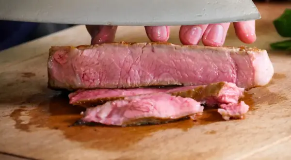 Ein saftiges Kalbskotelett sous vide wird auf einem Holzbrett in Scheiben geschnitten.