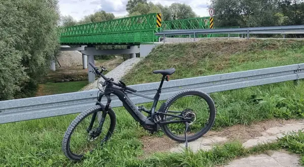 Rower elektryczny czeka na przygodę na trasie w Kazimierzu Dolnym. Zielony most w tle zaprasza do odkrywania malowniczych zakątków.